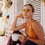 woman in stylish sunglasses and orange t-shirt sitting outside with coffee