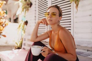 woman in stylish sunglasses and orange t-shirt sitting outside with coffee