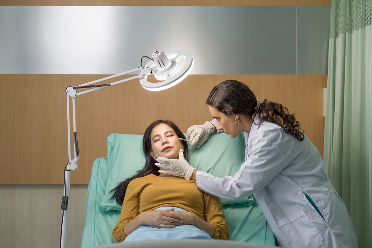 Doctor in white gown and protective glove giving female patient medical injection in temporal