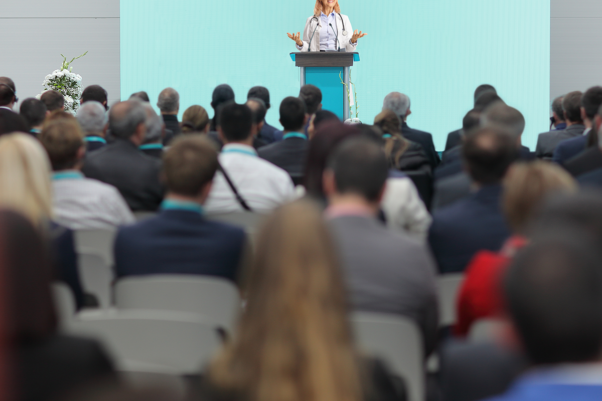 female doctor giving a speech on a pedestal in front of an audience